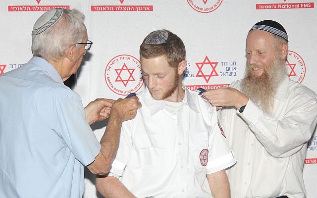 Dvir Shnerb receives shoulder epaulets from his father Rabbi Eitan Shnerb and his grandfather Zvi Wisbert, at the graduation ceremony of the MDA Medics Course. (Madagascar Photography via JTA)