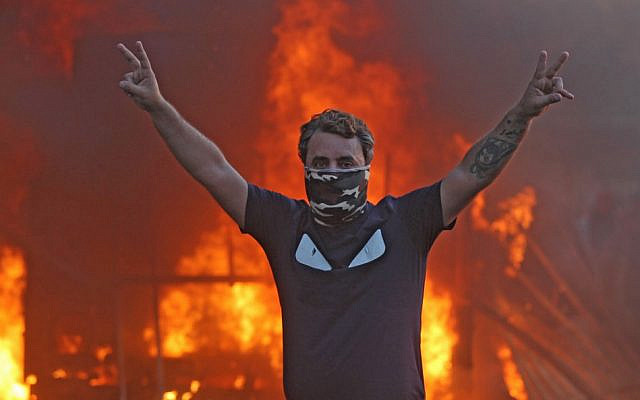 A protester flashes the V for victory sign as a riot police vehicle burns behind him during clashes amidst demonstrations against state corruption, failing public services, and unemployment in the Iraqi capital Baghdad's central Tayeran Square on October 3, 2019 (AHMAD AL-RUBAYE / AFP) A protester flashes the V for victory sign as a riot police vehicle burns behind him during clashes amidst demonstrations against state corruption, failing public services, and unemployment in the Iraqi capital Baghdad's central Tayeran Square on October 3, 2019 (AHMAD AL-RUBAYE / AFP)