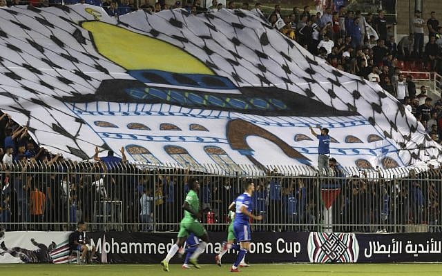 Spectators hold a huge flag depicting Jerusalem's Dome of the Rock shrine during a match between Palestinian team Hilal al-Quds and Morocco's Raja Casablanca in the Arab Champions Cup at Faisal Husseini stadium in the town of al-Ram, between Jerusalem and Ramallah, on October 3, 2019. (ABBAS MOMANI / AFP) Spectators hold a huge flag depicting Jerusalem's Dome of the Rock shrine during a match between Palestinian team Hilal al-Quds and Morocco's Raja Casablanca in the Arab Champions Cup at Faisal Husseini stadium in the town of al-Ram, between Jerusalem and Ramallah, on October 3, 2019. (ABBAS MOMANI / AFP)