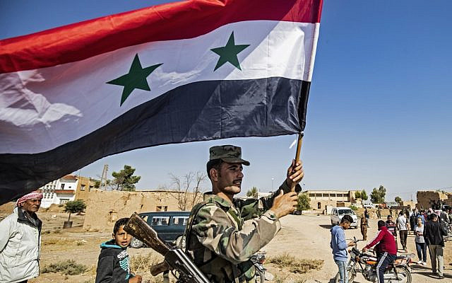 A Syrian regime soldier waves the national flag a street on the western entrance of the town of Tal Tamr in the countryside of Syria's northeastern Hasakeh province on October 14, 2019. (Delil SOULEIMAN / AFP)