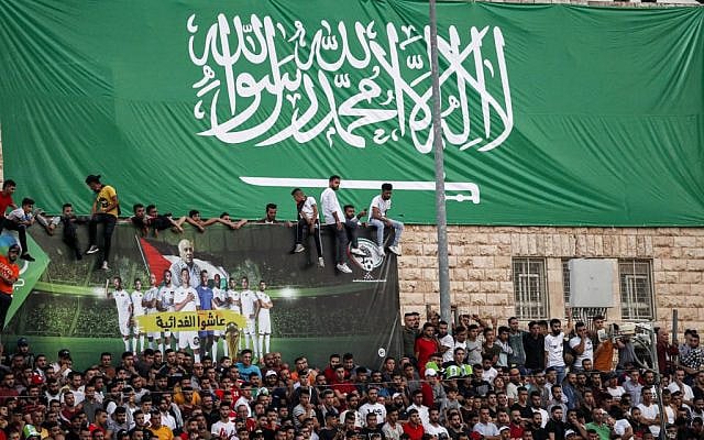 Football fans stand beneath a giant banner depicting the Saudi national flag as they attend the World Cup 2022 Asian qualifying match between Palestine and Saudi Arabia in the town of al-Ram in the West Bank on October 15, 2019. (Ahmad GHARABLI/AFP) Football fans stand beneath a giant banner depicting the Saudi national flag as they attend the World Cup 2022 Asian qualifying match between Palestine and Saudi Arabia in the town of al-Ram in the West Bank on October 15, 2019. (Ahmad GHARABLI/AFP)