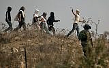 Illustrative: Israeli soldiers stand by as masked Israeli settlers throw stones at Palestinian protesters (unseen) gathering during a demonstration against construction on an Israeli outpost near the Palestinian village of Turmusaya and the settlement of Shilo, north of Ramallah in the West Bank, on October 17, 2019. (Jaafar Ashtiyeh/ AFP/ File)