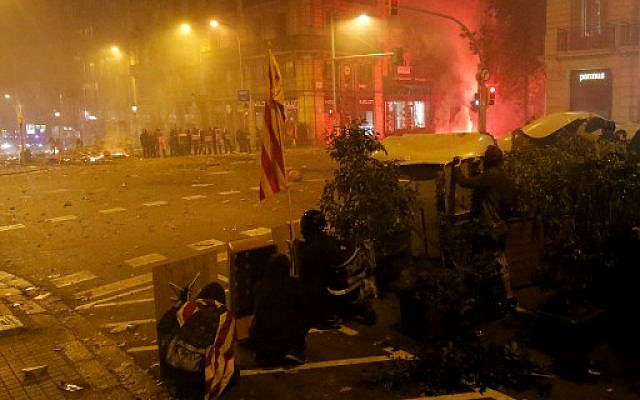 Protesters take shelter behind garbage containers during clashes near the Police headquarters in Barcelona, on October 18, 2019, on the day that separatists called a general strike and a mass rally. - Spain's protest-hit northeast was gripped by a general strike today as thousands of "freedom marchers" converged on Barcelona for a mass show of dissent over the jailing of nine Catalan separatist leaders. (Photo by Pau Barrena / AFP) Protesters take shelter behind garbage containers during clashes near the Police headquarters in Barcelona, on October 18, 2019, on the day that separatists called a general strike and a mass rally. - Spain's protest-hit northeast was gripped by a general strike today as thousands of "freedom marchers" converged on Barcelona for a mass show of dissent over the jailing of nine Catalan separatist leaders. (Photo by Pau Barrena / AFP)