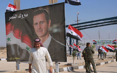 A man passes a poster of Syrian President Bashar Assad with Arabic that reads, 'Congratulations victory,' on September 30, 2019, while crossing the border into Syria at the newly opened crossing between the Iraqi town of Qaim and Syria's Boukamal, Syria. (AP Photo/Hadi Mizban, File)