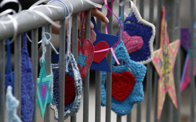 A woman ties hand-made hearts to a fence outside the Tree of Life synagogue in Pittsburgh on Sunday, Oct. 27, 2019, the first anniversary of the shooting at the synagogue, that killed 11 worshippers.(AP Photo/Gene J. Puskar)