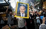 A Likud party supporter holds a campaign poster featuring then-prime minister Benjamin Netanyahu at Jerusalem's Mahane Yehuda market on April 7, 2019. (Yonatan Sindel/Flash90)