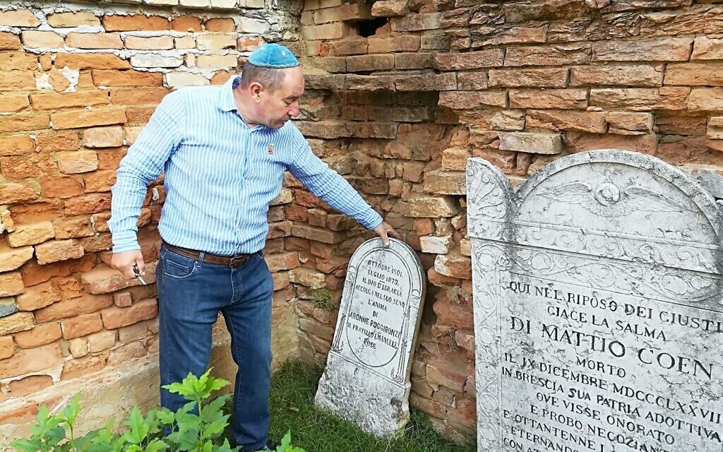 Giuseppe Minera grasps a tombstone next to the decaying stone and brick wall in the Jewish cemetery of Ostiano, Italy. (Giovanni Vigna/ Times of Israel)