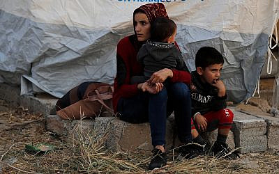 A Syrian woman with her children, who were displaced by the Turkish military operation in northeastern Syria, wait to receive a tent and other aid supplies at the Bardarash refugee camp, north of Mosul, Iraq, October 17, 2019. (AP Photo/Hussein Malla)