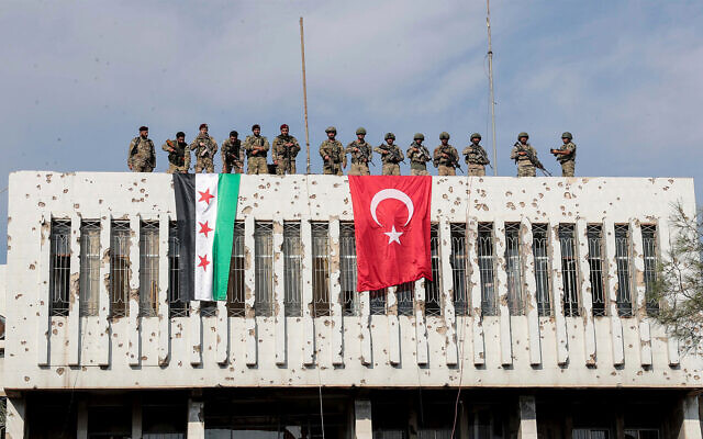 Turkish soldiers, right, and Turkey-backed opposition fighters, left, stand on a building next to their flags the town of Ras al Ayn in northeastern Syria, October 23, 2019. (Ugur Can/DHA via AP) Turkish soldiers, right, and Turkey-backed opposition fighters, left, stand on a building next to their flags the town of Ras al Ayn in northeastern Syria, October 23, 2019. (Ugur Can/DHA via AP)