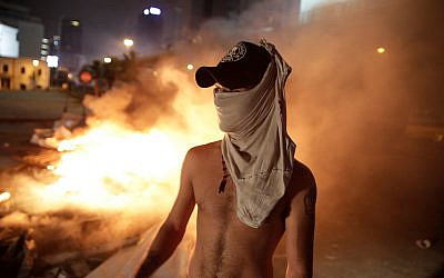 An anti-government protester stands by a fire of plastic barriers and trash blocking a road during a demonstration against corruption in Beirut, Lebanon, October 17, 2019.(AP  Photo/Hassan Ammar)
