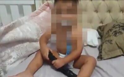An 18-month-old baby is filmed playing with a gun in his crib in the northern city of Umm al-Fahm. (screen capture: Kan public broadcaster)