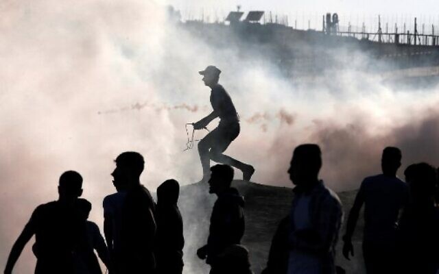 Palestinian rioters stand amid tear gas canisters fired by Israeli forces during clashes along the border with Israel east of Bureij in the central Gaza Strip on November 1, 2019. (Mahmud Hams/AFP) Palestinian rioters stand amid tear gas canisters fired by Israeli forces during clashes along the border with Israel east of Bureij in the central Gaza Strip on November 1, 2019. (Mahmud Hams/AFP)