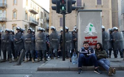 Lebanese anti-government protesters rest on a pavement in front of members of security forces in a central neighborhood of the capital Beirut on November 4, 2019 (Patrick BAZ / AFP)