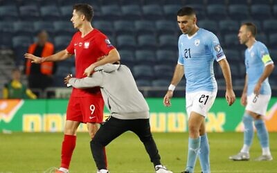 A man runs onto the field and hugs Poland's forward Robert Lewandowski on the pitch during the EURO 2020 group G qualifiers football match between Israel and Poland at the Teddy stadium in Jerusalem on November 16, 2019. He and a second invading fan were taken away by security guards. (Photo by Jack GUEZ / AFP)