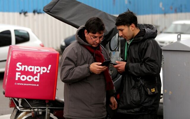 A bike-delivery food messenger stands next to another man as they both use smartphones along the side of a street in the Iranian capital Tehran on November 23, 2019. (Atta Kenare/AFP) A bike-delivery food messenger stands next to another man as they both use smartphones along the side of a street in the Iranian capital Tehran on November 23, 2019. (Atta Kenare/AFP)