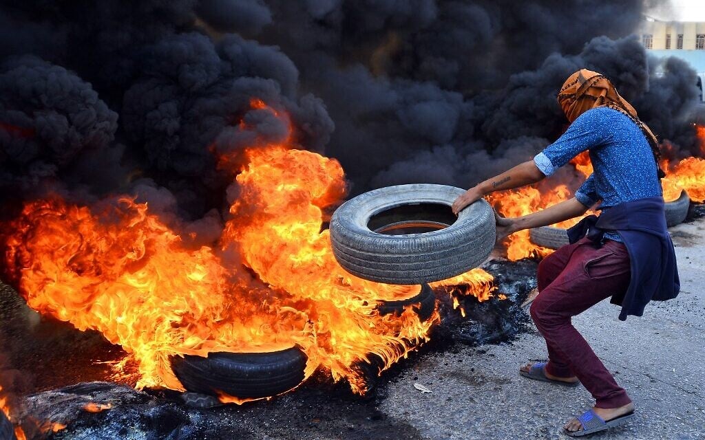 An Iraqi protester throws a tire on a stack of burning tires at a roadblock in the central holy shrine city of Najaf on November 26, 2019. (Haidar HAMDANI / AFP) An Iraqi protester throws a tire on a stack of burning tires at a roadblock in the central holy shrine city of Najaf on November 26, 2019. (Haidar HAMDANI / AFP)