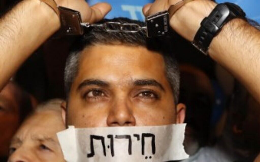 A supporter of Prime Minister Benjamin Netanyahu wearing handcuffs and covering his mouth with a sign reading in Hebrew: "freedom," at a rally held under the banner 'protesting the coup' in Tel Aviv, on November 26, 2019. (Jack Guez/AFP)