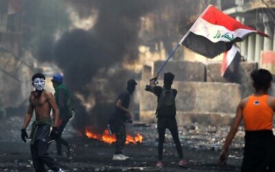 An Iraqi anti-government protester waves a national flag close to a concrete barricade amidst clashes with security forces along the capital Baghdad's Rasheed street near al-Ahrar bridge on November 29, 2019 (AHMAD AL-RUBAYE/AFP)