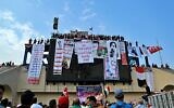 In this photo from October 30, 2019, Iraqi anti-government protesters hang their demands and slogans while standing on a building near Tahrir Square, Baghdad, Iraq. (AP Photo/Hadi Mizban)
