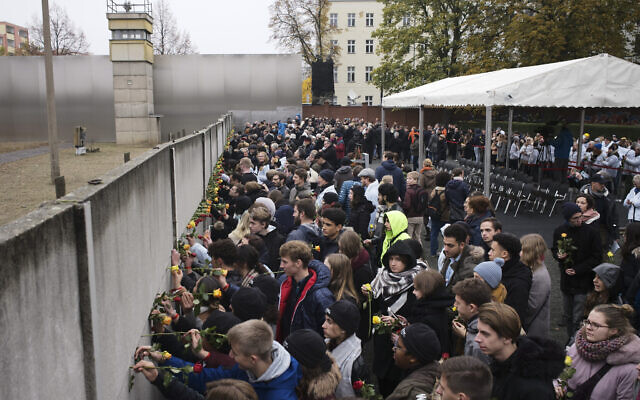 Young people stuck flowers in remains of the Berlin Wall during a commemoration ceremony to celebrate the 30th anniversary of the fall of the Berlin Wall at the Wall memorial site at Bernauer Strasse in Berlin,  Nov. 9, 2019. (AP Photo/Markus Schreiber)
