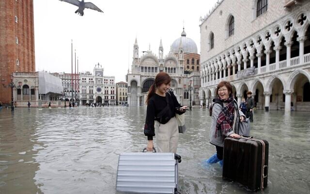 Tourists push their luggage in a flooded St. Mark's Square, in Venice, Nov. 13, 2019. (AP Photo/Luca Bruno)