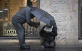 Illustrative. A man gives money to a homeless person, as he holds an umbrella to protect them both from the rain on Jaffa Street, Jerusalem, on November 3, 2014. (Yonatan Sindel/Flash90/File)