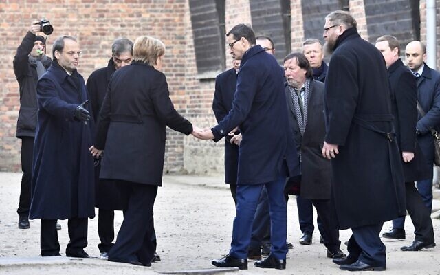German Chancellor Angela Merkel (C-L) and Polish Prime Minister Mateusz Morawiecki (C-R) join hands after laying wreathes at the Death Wall during their visit at the former German Nazi death camp Auschwitz-Birkenau in Oswiecim, Poland on December 6, 2019; at (L) is Felix Klein, the German government's Commissioner for Jewish Life in Germany, at (3rd-R) is the Director of the Auschwitz-Birkenau State Museum Piotr Cywinski and at (5th-R) is Christoph Heubner, executive vice-president of the International Auschwitz Committee. (John Macdougall/AFP)
