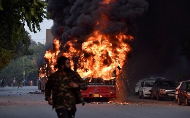 A man walks on a street as a bus is on fire following a demonstration against the Indian government's Citizenship Amendment Bill (CAB) in New Delhi on December 15, 2019. (STR / AFP) A man walks on a street as a bus is on fire following a demonstration against the Indian government's Citizenship Amendment Bill (CAB) in New Delhi on December 15, 2019. (STR / AFP)