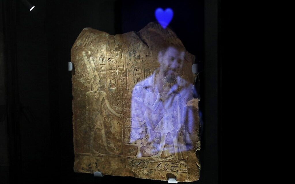 A video installation shows the image of a man with the emoji of a blue hart reflected on an ancient Egyptian plaque engraved with Hieroglyphs, at the exhibition "Emoglyphs: Picture-Writing from Hieroglyphs to the Emoji" at the Israel Museum in Jerusalem, on December 19, 2019. (MENAHEM KAHANA / AFP) A video installation shows the image of a man with the emoji of a blue hart reflected on an ancient Egyptian plaque engraved with Hieroglyphs, at the exhibition "Emoglyphs: Picture-Writing from Hieroglyphs to the Emoji" at the Israel Museum in Jerusalem, on December 19, 2019. (MENAHEM KAHANA / AFP)
