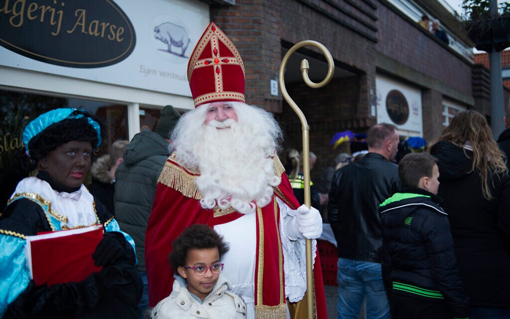 A man dressed like Sinterklaas and a woman portraying Black Pete entertain children under police protection in northern Amsterdam, the Netherlands, November 16, 2019. (Cnaan Liphshiz/JTA)