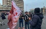A protester holds a blood-stained flag at the site of a gunmen attack in Baghdad, Iraq, Saturday, Dec. 7, 2019 (AP/Ali Abdul Hassan)