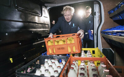 Britain's Prime Minister Boris Johnson loads a crate into a milk delivery van during a visit to Greenside Farm Business Park, as he campaigns for votes on the last day of campaigning ahead of a General Election, in Leeds, England, December 11, 2019.  (Stefan Rousseau/PA via AP)