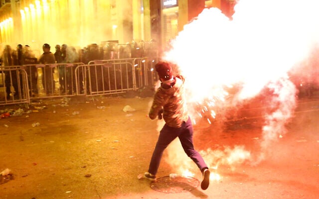 An anti-government protester throws flares against the riot police, background, during a protest near the parliament square, in downtown Beirut, Lebanon, Sunday, Dec. 15, 2019. Lebanese security forces fired tear gas, rubber bullets and water cannons Sunday to disperse hundreds of protesters for a second straight day, ending what started as a peaceful rally in defiance of the toughest crackdown on anti-government demonstrations in two months. (AP Photo/Hussein Malla)