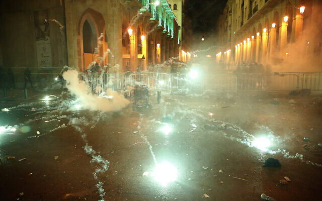 Anti-government protesters throw firecrackers against the riot police, background, during a protest near the parliament square, in downtown Beirut, Lebanon, Sunday, Dec. 15, 2019.  (AP Photo/Hussein Malla)