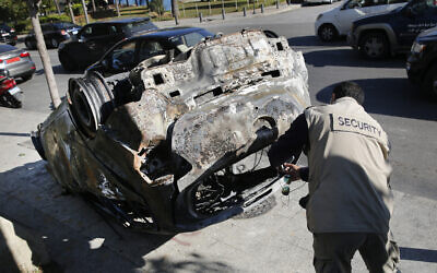 A private security worker takes pictures of a burned car that was set on fire by supporters of the Shiite Hezbollah and Amal Movement groups, in Beirut, Lebanon, December 17, 2019. (Hussein Malla/AP)