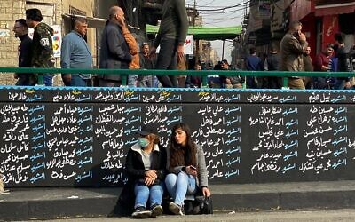 Women sit by a wall with names of nti-government protesters who have been killed in demonstrations in Tahrir Square during ongoing protests in Baghdad, Iraq, December 12, 2019. (AP Photo/Nasser Nasser)