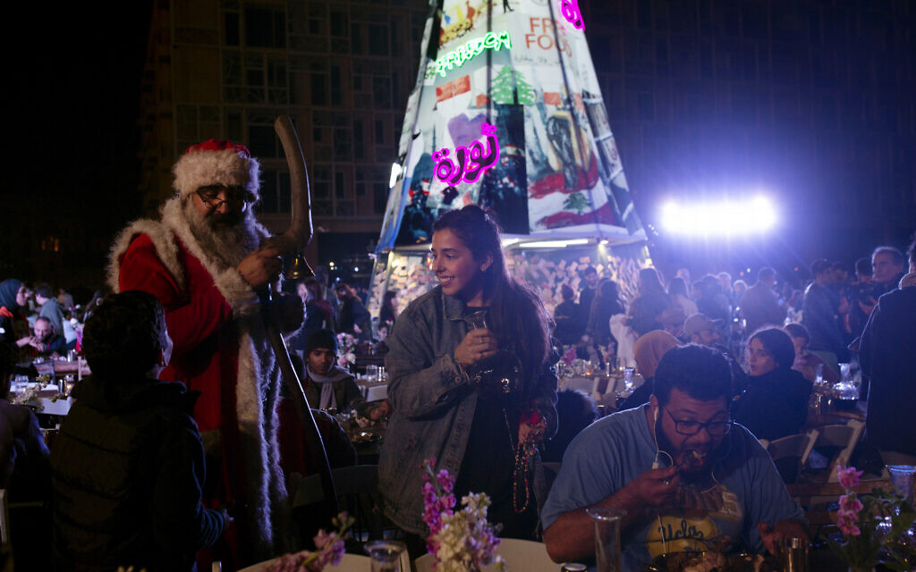 In this Monday, December 23, 2019 photo, a volunteer, center, serves drinks at a public Christmas dinner as a boy asks Santa Claus for a selfie, in Martyrs Square where anti-government activists are encamped, in Beirut, Lebanon. (AP Photo/Maya Alleruzzo) In this Monday, December 23, 2019 photo, a volunteer, center, serves drinks at a public Christmas dinner as a boy asks Santa Claus for a selfie, in Martyrs Square where anti-government activists are encamped, in Beirut, Lebanon. (AP Photo/Maya Alleruzzo)