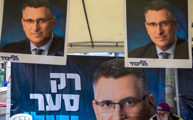 A Likud party member sits by a poster of veteran politician Gideon Saar from the governing Likud Party at a voting center in the northern Israeli city of Hadera,on December 26, 2019. (AP/Ariel Schalit)