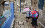 Illustrative: People walk in the rain in the northern Israeli city of Sefad, on a stormy winter day, December 9, 2019. (David Cohen/ Flash90)
