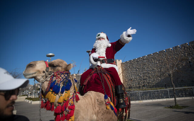 A man dressed as Santa Claus rides a camel at Jaffa Gate in Jerusalem's Old City, during Christmas tree distribution and a few days before the upcoming holiday of Christmas, December 19, 2019. (Yonatan Sindel/Flash90) A man dressed as Santa Claus rides a camel at Jaffa Gate in Jerusalem's Old City, during Christmas tree distribution and a few days before the upcoming holiday of Christmas, December 19, 2019. (Yonatan Sindel/Flash90)