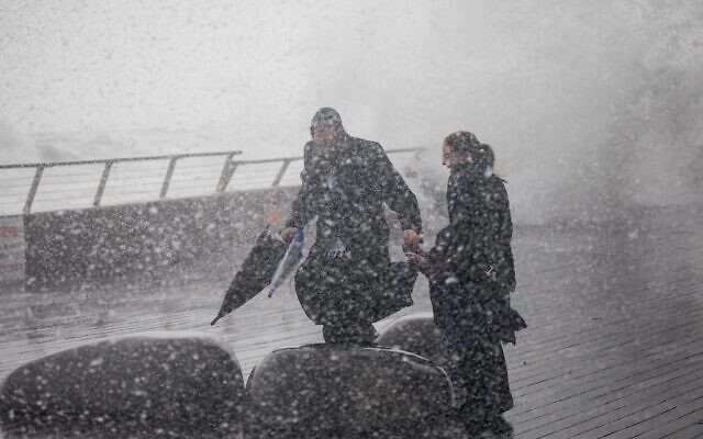 A family runs from large waves during a stormy day at the Tel Aviv Port, December 26, 2019. (Yonatan Sindel/Flash90)