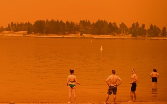 Residents take a dip to cool down at Lake Jindabyne, under a red sky due to smoke from bushfires, in the town of Jindabyne in New South Wales on January 4, 2020 (Saeed KHAN / AFP)