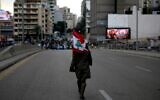 A woman carrying a national flag walks toward Lebanese demonstrators blocking the main bridge linking the western and eastern sides of the capital Beirut, to protest against a political elite accused of corruption and incompetence, on Janury 17, 2020.  (Photo by PATRICK BAZ / AFP)