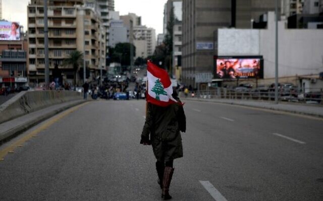 A woman carrying a national flag walks toward Lebanese demonstrators blocking the main bridge linking the western and eastern sides of the capital Beirut, to protest against a political elite accused of corruption and incompetence, on Janury 17, 2020. (Photo by PATRICK BAZ / AFP) A woman carrying a national flag walks toward Lebanese demonstrators blocking the main bridge linking the western and eastern sides of the capital Beirut, to protest against a political elite accused of corruption and incompetence, on Janury 17, 2020. (Photo by PATRICK BAZ / AFP)