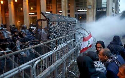 Lebanese anti-government protesters gather by the barricaded road leading to parliament in central Beirut as smoke billows from tear gas canisters, on January 19, 2020 . (PATRICK BAZ/AFP)
