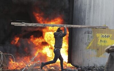 A Palestinian carries a ladder past a fire by the Israeli security barrier in the West Bank village of Bilin near Ramallah on January 31, 2020, during clashes with Israeli security forces over the US-brokered proposal for a settlement of the Israeli-Palestinian conflict. (Abbas Momani/AFP)