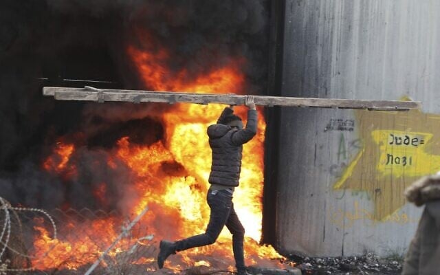 A Palestinian carries a ladder past a fire by the Israeli security barrier in the West Bank village of Bilin near Ramallah on January 31, 2020, during clashes with Israeli security forces over the US-brokered proposal for a settlement of the Israeli-Palestinian conflict. (Abbas Momani/AFP) A Palestinian carries a ladder past a fire by the Israeli security barrier in the West Bank village of Bilin near Ramallah on January 31, 2020, during clashes with Israeli security forces over the US-brokered proposal for a settlement of the Israeli-Palestinian conflict. (Abbas Momani/AFP)