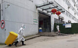 In this January 23, 2020, photo, a staff member wearing a hazardous materials suit hauls a bin at a hospital that reported a coronavirus death in Yichang in central China's Hubei Province.  (Chinatopix via AP)