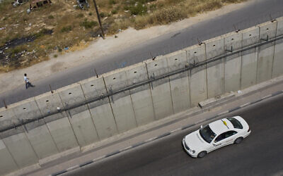 Illustrative: A Palestinian man walks along Israel's security barrier, in the West Bank town of Aram, as a taxi drives in the East Jerusalem neighborhood of Beit Hanina, May 24, 2011.  (AP Photo/Bernat Armangue)