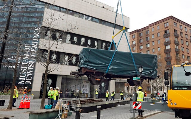 Portraits of Holocaust survivors are displayed at the Museum of Jewish Heritage, as a vintage German train car, like those used to transport people to Auschwitz and other death camps, is lowered onto tracks outside the museum in New York, March 31, 2019. (AP/Richard Drew) Portraits of Holocaust survivors are displayed at the Museum of Jewish Heritage, as a vintage German train car, like those used to transport people to Auschwitz and other death camps, is lowered onto tracks outside the museum in New York, March 31, 2019. (AP/Richard Drew)
